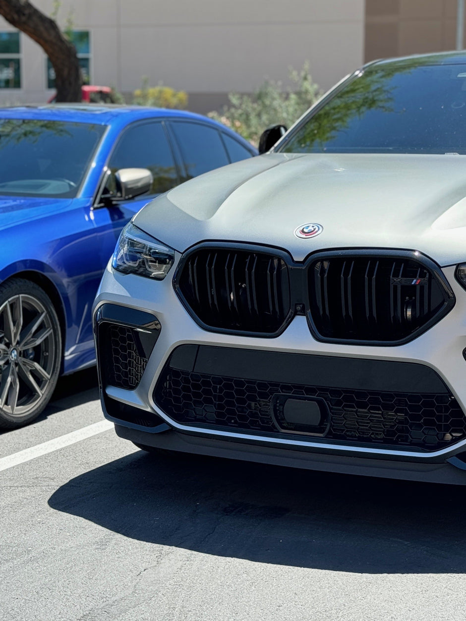 Two BMW cars, one blue and one silver, parked side by side on a street.