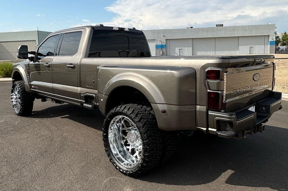 Bronze pickup truck with large wheels on a paved surface under a blue sky.