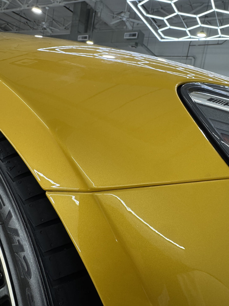 Close-up of a yellow car's side panel in a showroom setting