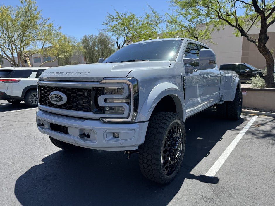 White Ford truck parked in a lot with trees and buildings in the background