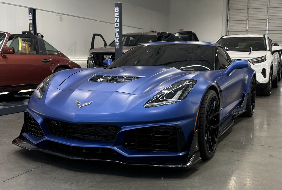 Blue Corvette in a showroom with other vehicles in the background