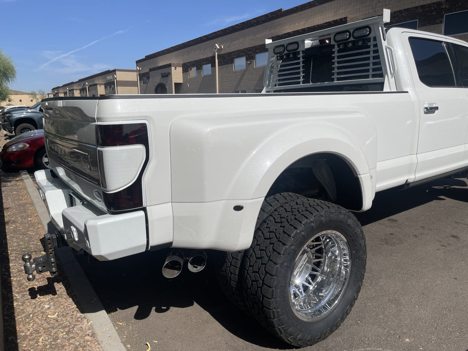 White pickup truck with large tires and a chrome bumper on a street.