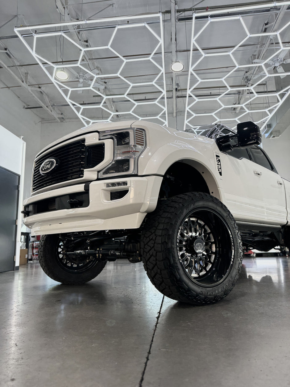 White Ford truck with large off-road tires in a showroom setting